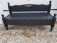 Front view of black wooden bench with metal Harley Davidson logo on backrest and silver tacks along the seat trim.
