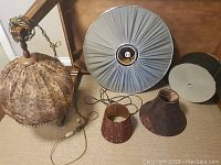 Photo showing five hanging lamps and lamp shades including animal print beaded lamp, grey pleated lamp, mounted 3 light fixture with patterned shade, and two smaller new shades.