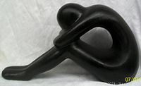 Side view of the large dark glazed pottery nude sculpture showing elongated leg and head shape with curved arm creating negative space