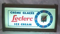 Front view of illuminated rectangular advertising sign reading Crème Glacée Leclerc Ice Cream with round clock dial on right side showing time. Dark wood frame.