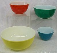 Full view of the four multicolored Pyrex mixing bowls arranged on clear risers showing size and color contrast