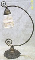 Side view of decorative reading lamp showing ornate metal base and curved arm with glass shade attached.