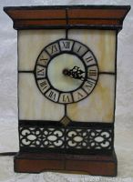Front view of stained glass lamp with visible clock face, clock shows time with Roman numerals and black decorative hands. Lamp off showing colored glass panels.