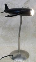 Side view of black airplane-shaped reading light on circular metal base, light illuminated.