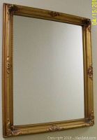 Front view of the antique gilt framed mirror with ornate floral and scroll decorations at the corners and sides.
