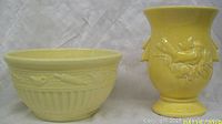 Yellow glazed ceramic bowl with embossed birds and vertical fluting and yellow glazed vase with floral relief and flared top, both shown side by side.