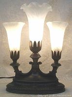 Front view of lamp illuminated, showing three fluted glass shades on metal base