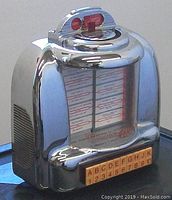 Front left angle view showing the chrome finish, speaker grill, illuminated panel with song list and keypad below.