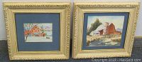 Pair of framed paintings by Earl Phillips showing barns in winter landscapes, both framed in gold frames with blue mats.