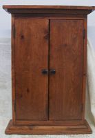 Front view of closed wood cabinet with two doors and black round knobs.