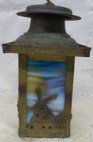 Close view of stained glass panel depicting a windmill in front of a blue and yellow sky, surrounded by metal framework with a patina finish.