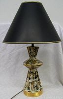 Full front view of the lamp with black shade and speckled ceramic base.