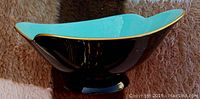 Side view of the footed bowl showing black exterior, turquoise interior with gold rim and pedestal base.