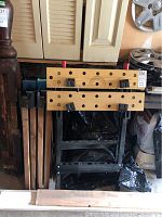 Workbench with wooden top and metal frame, viewed folded with sawhorse legs stacked.