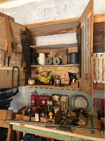 Wooden cabinet with open doors revealing various large hand saws, wiring spools, measuring tape, and miscellaneous tools.