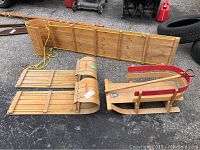 Three wooden sleds placed outdoors on asphalt, showing the full length profile of the toboggan, Torpedo sled, and segmented sled.