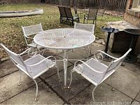 White wrought iron round mesh patio table and four matching chairs set on concrete patio