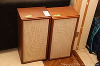 Front view of both wood veneer speaker cabinets with beige cloth grilles.