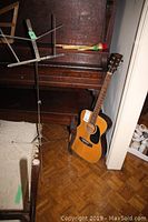Guitar leaning against piano next to music stand with maraca on piano