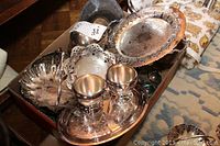 Photo showing assortment of silver plated trays, footed creamer and sugar bowl, candy dishes with ornate pierced edges and handles, displayed in a large tray.