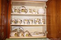 Three-tier cabinet showing assorted mugs, bowls, teapot and lidded pieces on shelves.