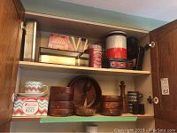Photo of cabinet shelves showing wooden bowls and tin boxes inside.