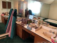 Photo showing Kenmore Ultra Stitch 12 sewing machine on a bathroom counter surrounded by sewing supplies including thread spools, scissors, and bobbins.