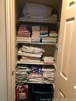 Full view of closet shelves with several stacks of assorted towels, bed linens in solid colors and floral prints.