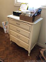 Baronet dresser cream color, with four drawers and ornate brass handles, wooden parquet floor background. Items on dresser not included.