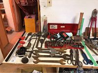 Full view of all vintage hand tools and electric drill, including wrenches, clamps, shears, mallets, and sockets on table surface.