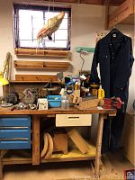 Full view of workbench with various tools, paint brushes, car parts, clamp, oil can, flashes, and hanging navy blue Todd brand overalls size 44R