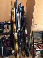 Full view of all skis standing upright showing various brands and colors along with ski boots and poles nearby.