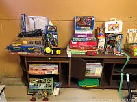 Wide view of the lot showing various boxed games and toys on a shelf, includes Batman Batmobile box, TMNT poster, He-Man game, and others.