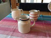 Three small ceramic pitchers placed on a colorful tablecloth, visible stripes and ribbed texture on pitchers