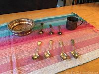 Overview of spoons, cup and bowl arranged on a colorful woven cloth.