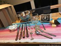 Overview of all kitchen items laid out on a striped cloth, showing knives, ice bucket, glass, scale, and various utensils.