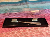 Full lot view of sterling silver toothbrush on black stand with two replacement heads and clear plastic cover.