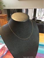 Front view of the delicate gold necklace displayed on a black jewelry bust showing the full length and fine chain detail.