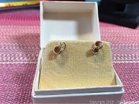 Front view of the gold knot earrings placed on a cream colored holder inside a white box without lid.