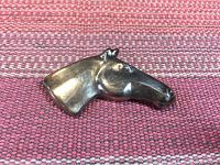 Close-up photo of the silver horse head brooch showing the left profile on a textured pink and white striped fabric background.