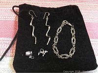 Full set of sterling silver jewelry laid out on black velvet pouch showing bracelet, earrings, and two charms.