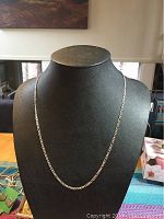 Front view of the 24 inch sterling silver Figaro link chain necklace displayed on a black bust stand.
