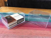Plastic case containing a stack of Yu-Gi-Oh cards mostly with backs facing up, showing standard card wear, inside a clear display box on a pink and blue patterned cloth.