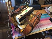 Singer sewing machine with yellow knobs in a brown carrying bag on a table with a colorful striped cloth.