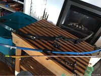 Photo of two bows (one black, one blue), one arrow, and accessories on a striped wooden table
