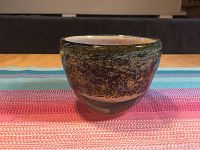 Full front view of the signed art glass bowl on a striped textile surface.