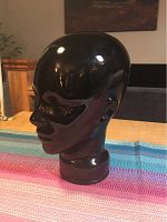 Left side view of the black glossy glass head bust on a multicolor striped fabric