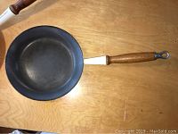 View of one frying pan showing dark interior cooking surface and wooden handle with metal loop end.