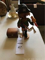 Side and back view of Steinbach pirate music box figurine with treasure chest next to it on table.