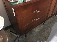 Side view showing wooden buffet cabinet with three drawers, metal handles, standing on round legs.